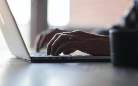 Typing on a laptop, dimly lit, focus on hands.